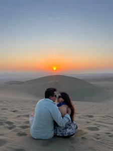 Paul y Carito sentados en la arena viendo el atardecer sobre las dunas de Huacachina