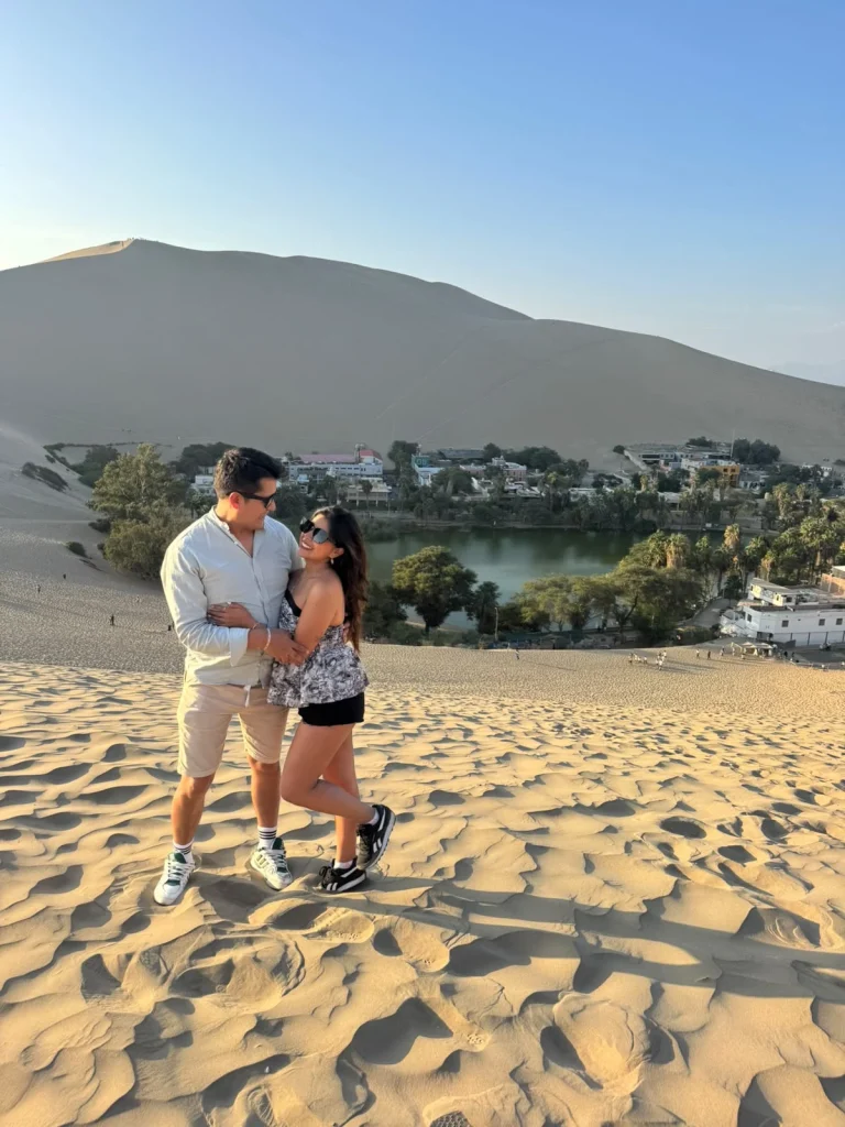 Paul y Carito sobre una duna con el oasis de Huacachina al fondo, en Ica